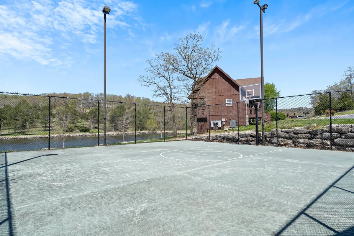 A scenic basketball court situated near a lake, surrounded by nature and with a cozy cabin-style house in view. The setting is ideal for outdoor sports, lakeside picnics, and exploring nature trails with the family.