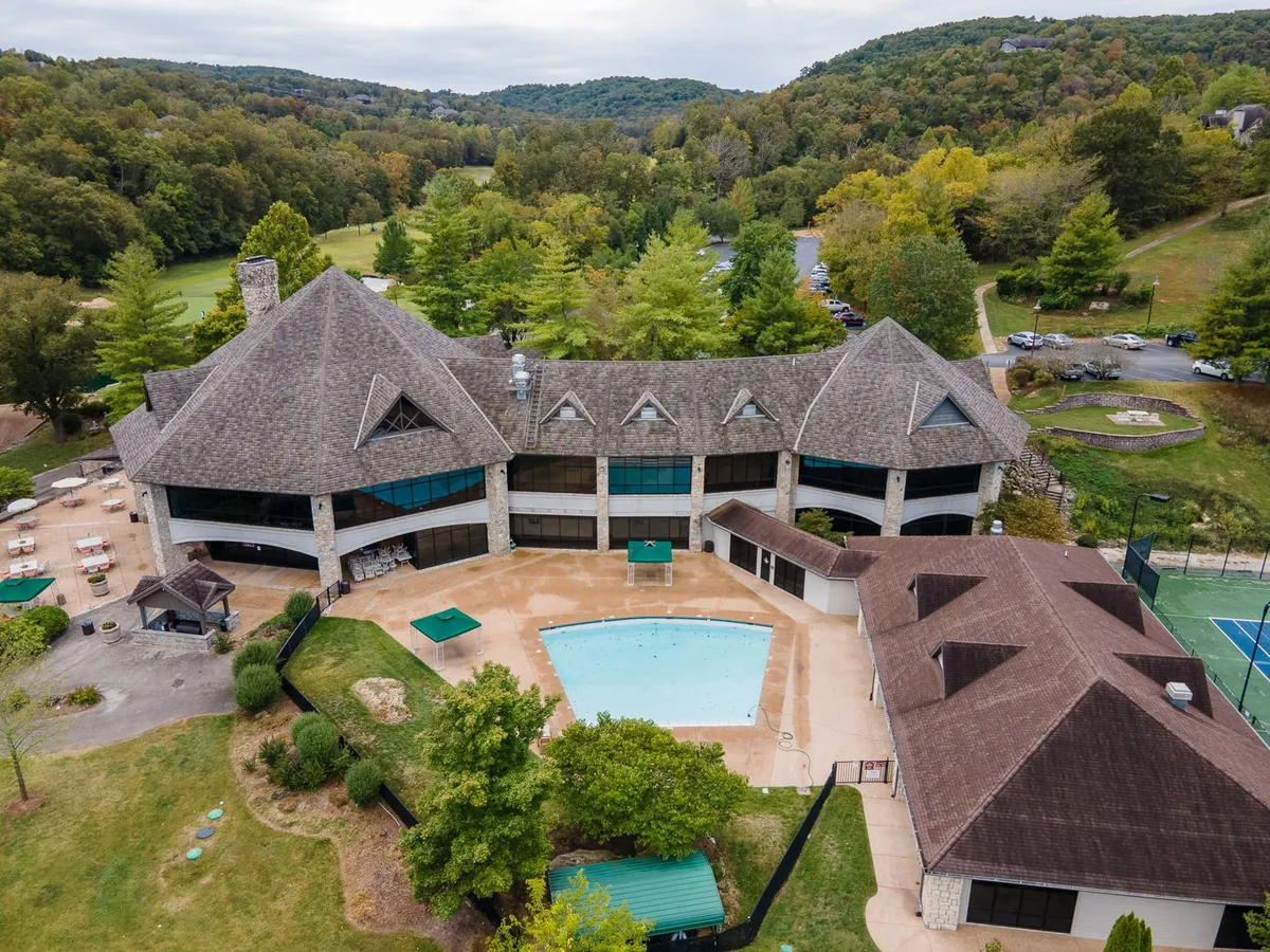 A sparkling outdoor swimming pool set among landscaped gardens and modern architecture, with a tennis court visible in the background. Lounge chairs line the pool, and the area is surrounded by lush greenery, creating an inviting space for summer relaxation and social gatherings.