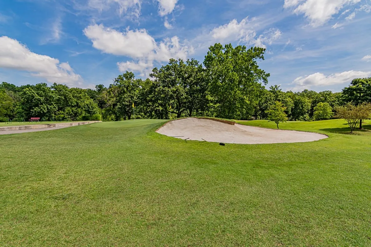 A panoramic view of a lush, green golf course bordered by thick trees and set under a clear blue sky. The perspective shows the open expanse of the fairway and the natural beauty of the Ozarks, emphasizing the setting that guests will enjoy from their balcony.