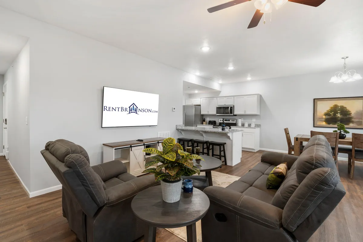 A warm, inviting interior featuring a stylish sofa seating area, a visible kitchen counter, a dining table, and a television. The open layout connects the kitchen, dining, and living zones, emphasizing comfort and the togetherness of shared experiences.