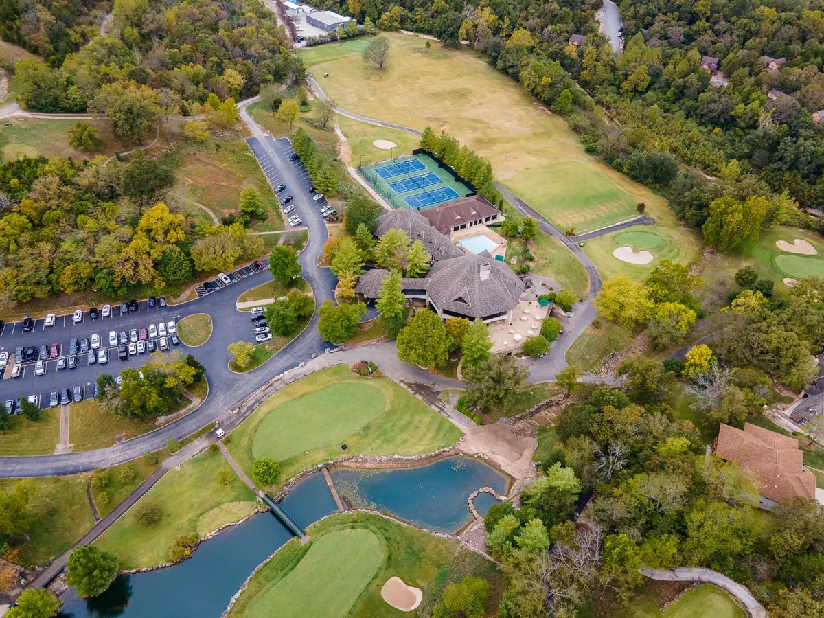 This exterior image showcases the Ledgestone Golf Course in the foreground, with adjacent tennis courts, the main resort building, parking area, and serene water features visible. Golfers can be seen out on the lush, rolling greens, embodying the active spirit of a golf getaway while the surrounding natural landscape emphasizes the scenic beauty of the Ozarks.