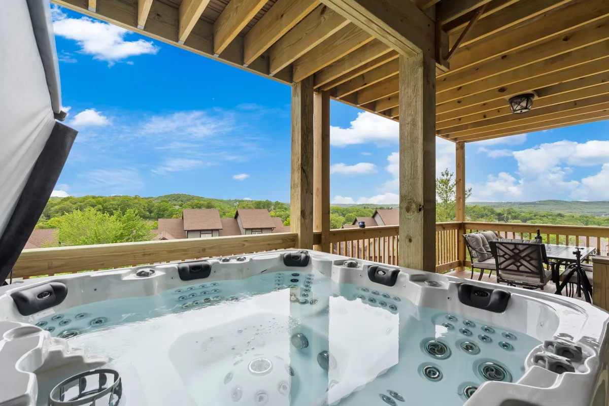 This image features a tranquil outdoor balcony area with a private hot tub, comfortable seating, and an expansive scenic view of green fairways and rolling hills. The setting is peaceful, with the sun low on the horizon, suggesting either sunrise or sunset and highlighting the resort-like atmosphere.