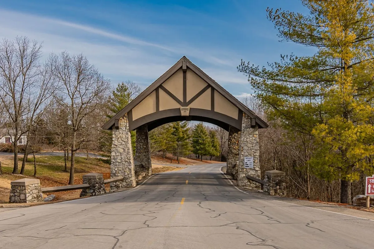 This image features an arched stone entrance with a tree-lined road, signifying entry into a private, exclusive community. The peaceful setting, greenery, and welcoming design reinforce the feeling of security and seclusion.