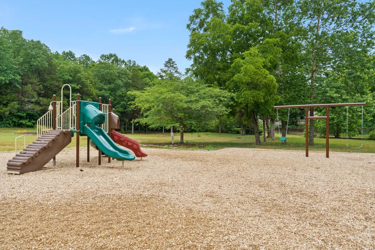 A vibrant playground scene with swings and various play structures, surrounded by trees. Children are visible playing and families gather around, evoking a sense of joyful community and play.